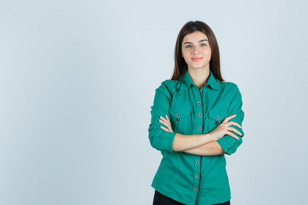 Belle jeune femme tenant les bras croisés en chemise verte et à la recherche positive. vue de face.