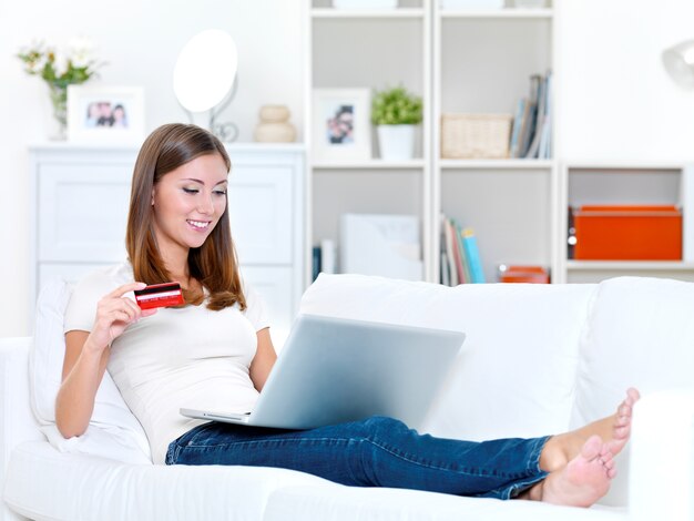 Belle jeune femme tenant une carte de crédit et regarde dans l'ordinateur portable - à l'intérieur