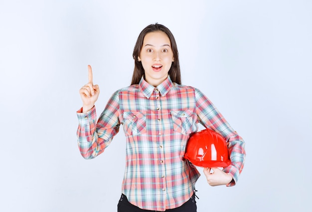 Belle jeune femme tenant un casque rouge et pointant sur fond blanc.