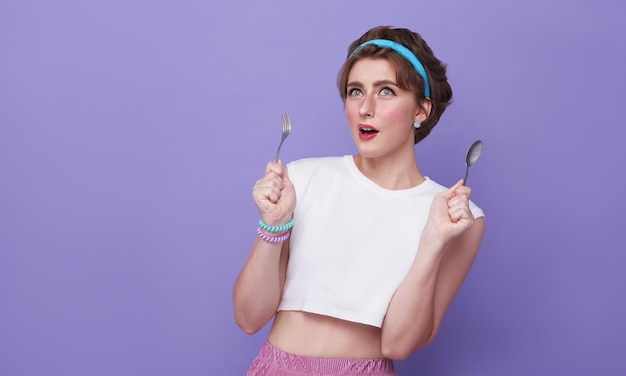 Belle jeune femme tenant une cuillère et une fourchette prêtes à manger isolées sur fond violet