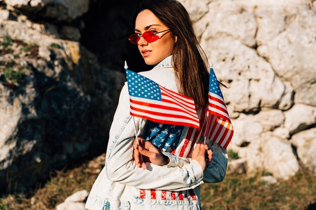 Belle jeune femme tenant des drapeaux américains dans les montagnes