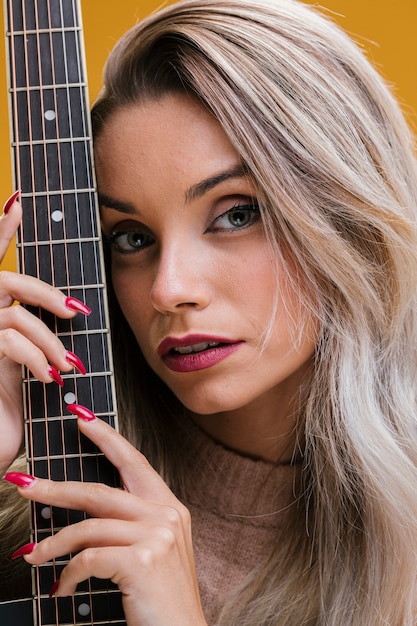 Belle jeune femme tenant une guitare sur fond jaune