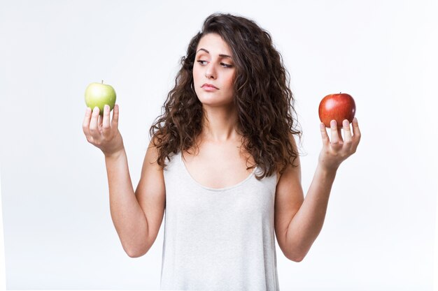 Belle jeune femme tenant des pommes vertes et rouges sur fond blanc.