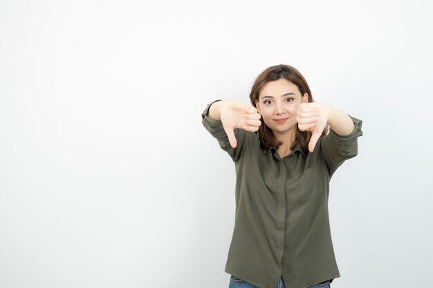 Belle jeune femme en tenue décontractée debout et donnant les pouces vers le bas. Photo de haute qualité