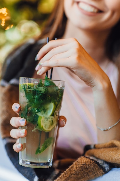 Belle jeune femme sur une terrasse d'été dans des vêtements décontractés boit un cocktail. Couvert d'une couverture