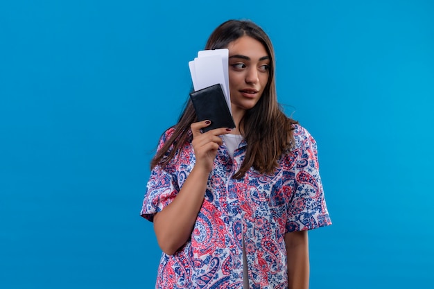 Photo gratuite belle jeune femme touriste tenant un passeport avec des billets à côté avec une expression sérieuse confiante sur mur bleu isolé