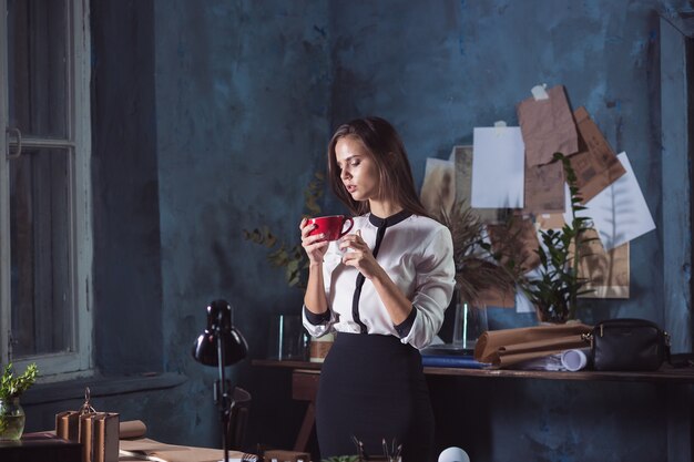 Belle jeune femme travaillant avec une tasse de café et un ordinateur portable au bureau loft