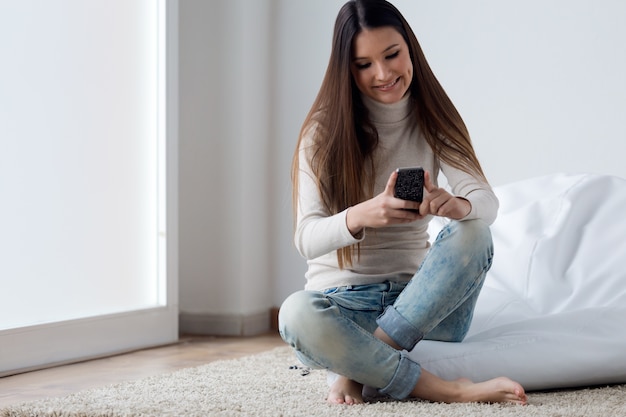 Belle jeune femme utilisant son téléphone mobile à la maison.