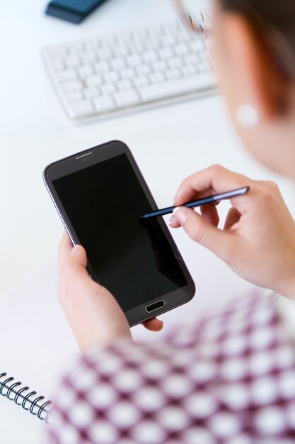 Belle jeune femme utilisant son téléphone portable au bureau.