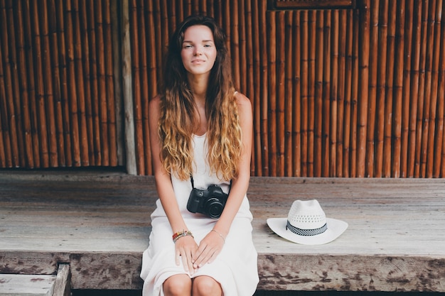 Belle jeune femme en vacances tropicales en Asie, style d'été, robe boho blanche, baskets, appareil photo numérique, voyageur, chapeau de paille, souriant, boho