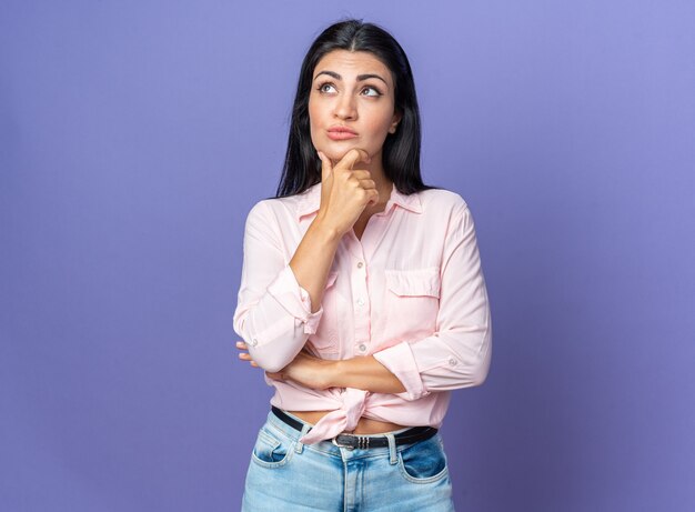 Belle jeune femme en vêtements décontractés levant la main sur le menton pensant avec une expression pensive