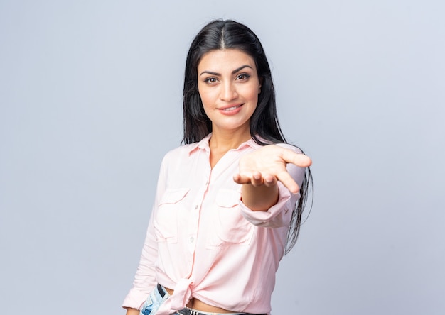 Belle jeune femme en vêtements décontractés à la recherche de sourire confiant faisant venir ici le geste avec la main