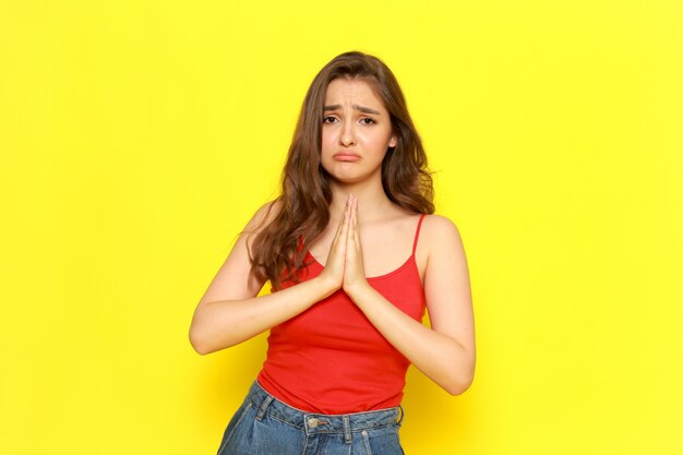 Une belle jeune femme vue de face en chemise rouge et jean bleu posant avec expression de mendicité