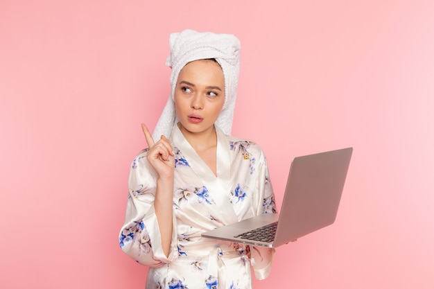 Une belle jeune femme vue de face en peignoir travaillant avec un ordinateur portable