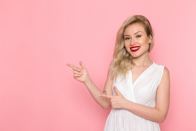 Une belle jeune femme vue de face en robe blanche posant avec le sourire sur son visage