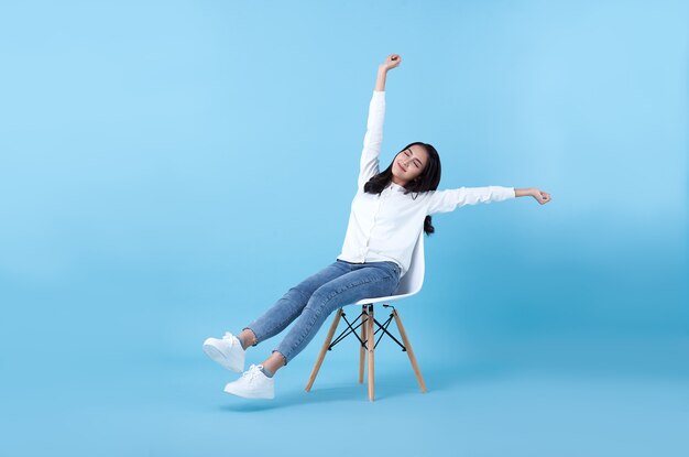 Belle jeune fille asiatique souriante se détendre assis sur une chaise sur bleu.