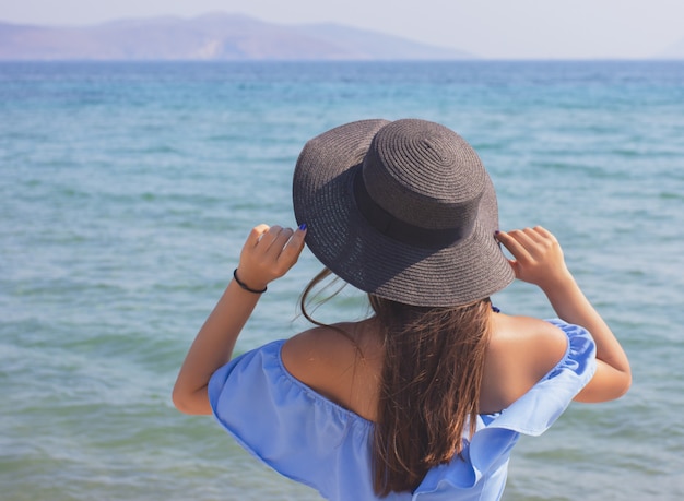 Belle jeune fille au chapeau regarde la mer