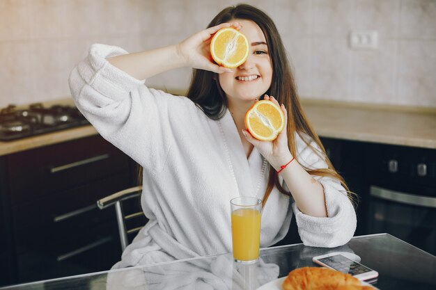 belle jeune fille aux cheveux noirs et robe blanche assis à la maison dans la cuisine à la table