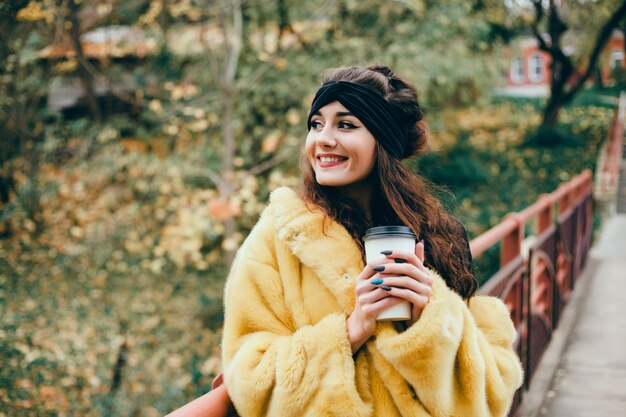 belle jeune fille boit du café dans un verre dans la rue, rit et sourit