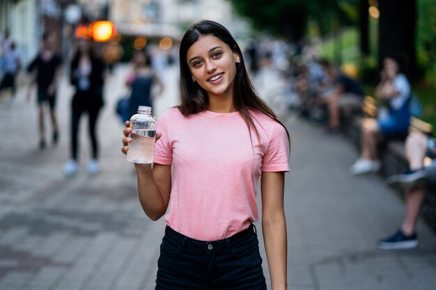 Belle jeune fille avec une bouteille d'eau dans une rue de la ville