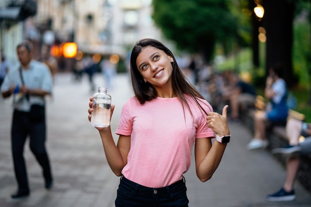 Belle jeune fille avec une bouteille d'eau dans une rue de la ville