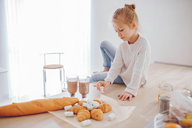 une belle jeune fille avec des cheveux clairs en dentelle blanche et un pantalon bleu jeans assis à la maison