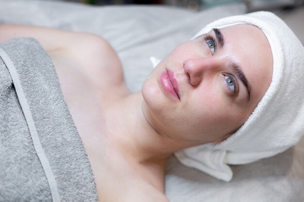 Une belle jeune fille est allongée sur la table de l'esthéticienne et reçoit des procédures, un léger massage du visage à l'huile.