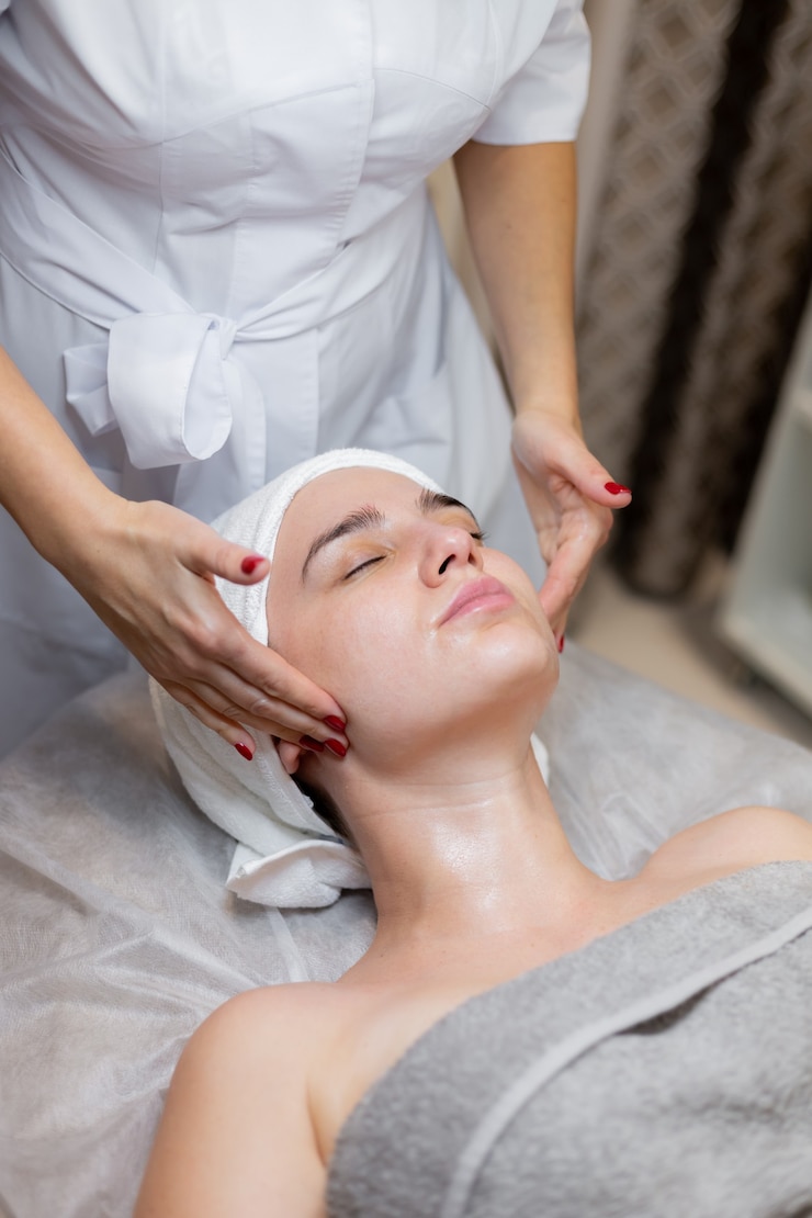 Photo gratuit une belle jeune fille est allongée sur la table de l'esthéticienne et reçoit des procédures, un léger massage du visage à l'huile.