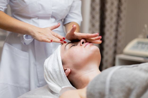 Une belle jeune fille est allongée sur la table de l'esthéticienne et reçoit des procédures, un léger massage du visage à l'huile.