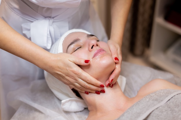 Une belle jeune fille est allongée sur la table de l'esthéticienne et reçoit des procédures, un léger massage du visage.