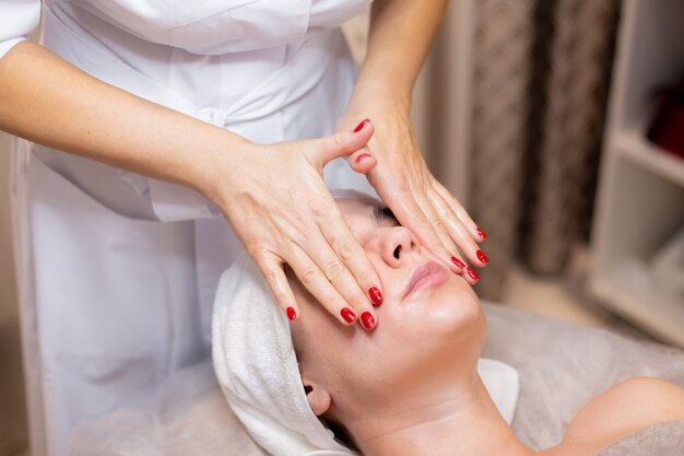 Une belle jeune fille est allongée sur la table de l'esthéticienne et reçoit des procédures, un léger massage du visage.