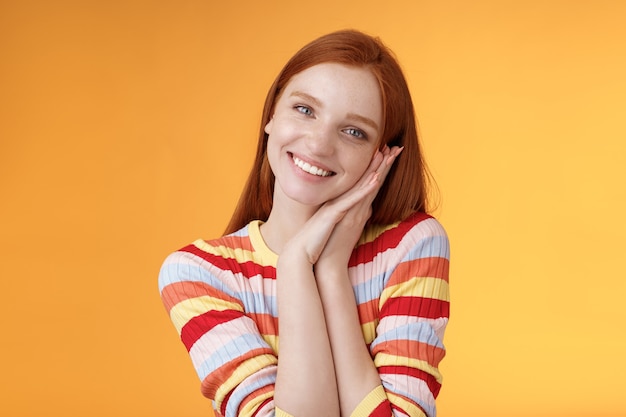 Belle jeune fille européenne rousse séduisante souriante largement excitée heureuse paume maigre recevoir doux tendre présent regard reconnaissant amusé réagissant joyeusement moment agréable, debout fond orange.