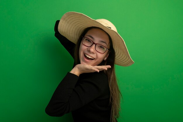 Belle jeune fille portant un chapeau d'été dans un col roulé noir et des lunettes heureux et positif
