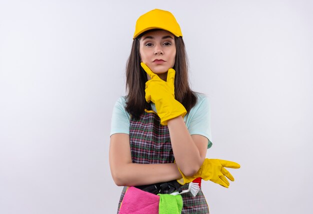 Belle jeune fille portant un tablier, une casquette et des gants en caoutchouc regardant la caméra avec la main sur le menton à la confiance