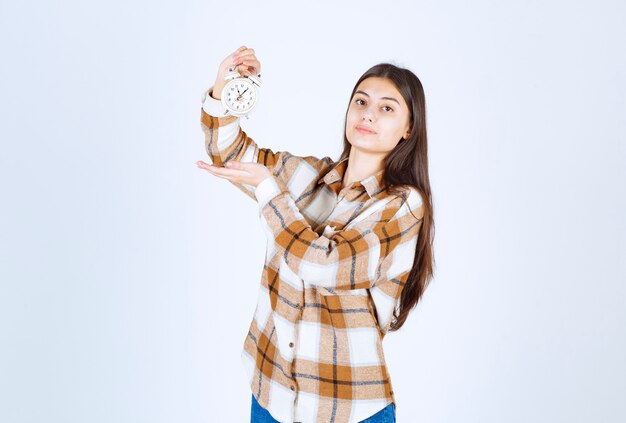 Belle jeune fille portant des vêtements décontractés indiquant l'heure sur le réveil.