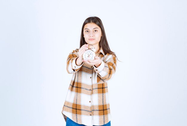 Belle jeune fille portant des vêtements décontractés montrant un réveil.