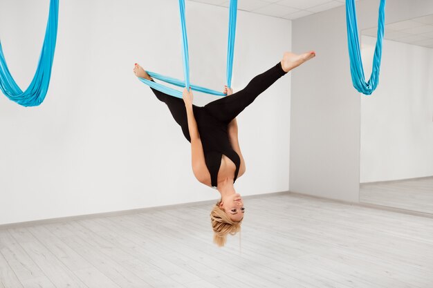 Belle jeune fille pratiquant le yoga aérien dans la salle de gym.