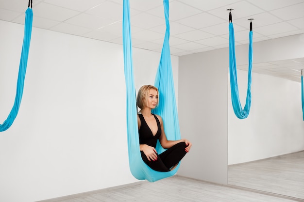 Belle jeune fille pratiquant le yoga aérien dans la salle de gym.