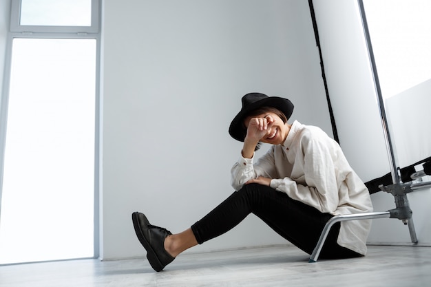 Belle jeune fille riant assis sur le plancher sur le mur blanc.