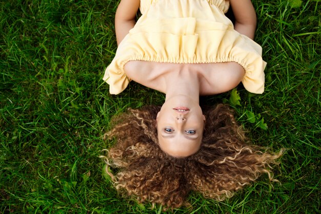 Belle jeune fille en robe jaune allongée sur l'herbe.