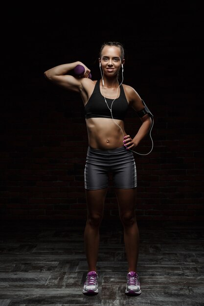 Belle jeune fille sportive souriante, formation sur mur sombre