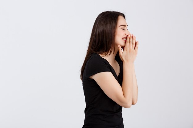 Belle jeune fille surprise en t-shirt noir posant sur un mur blanc