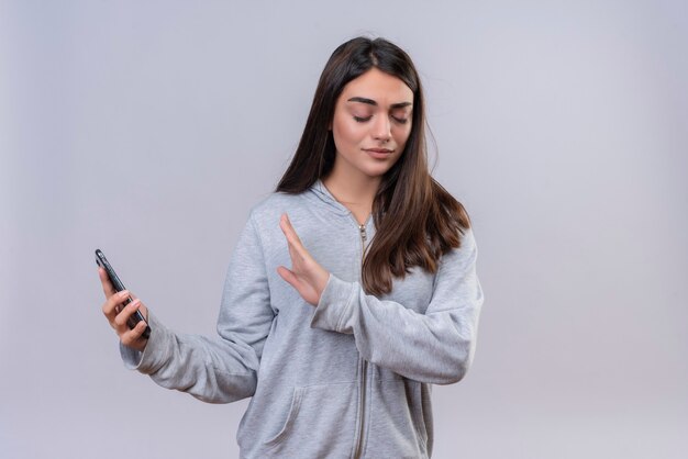 Belle jeune fille en sweat à capuche gris tenant le téléphone ne cherche pas à téléphone debout sur fond blanc