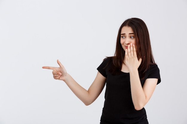 Belle jeune fille en t-shirt noir, pointant les doigts sur le côté sur le mur blanc