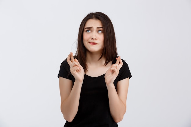 Belle jeune fille en t-shirt noir posant avec, espérons-le, les doigts croisés sur le mur blanc