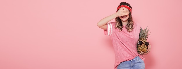 Belle jeune fille en t-shirt rose, couvre son visage, tient l'ananas