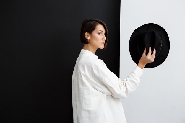 Belle jeune fille tenant un chapeau sur un mur noir et blanc