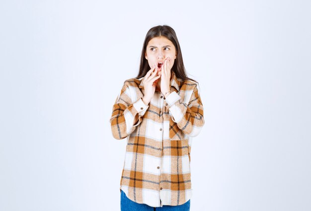 belle jeune fille en tenue décontractée posant sur un mur blanc.