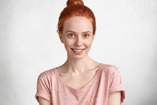 Photo gratuite belle jeune mannequin rousse souriante adorable habillée avec désinvolture, n'a pas de maquillage, démontre sa beauté naturelle, heureuse d'être photographiée