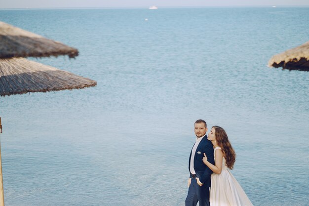 belle jeune mariée aux cheveux longs en robe blanche avec son jeune mari sur la plage